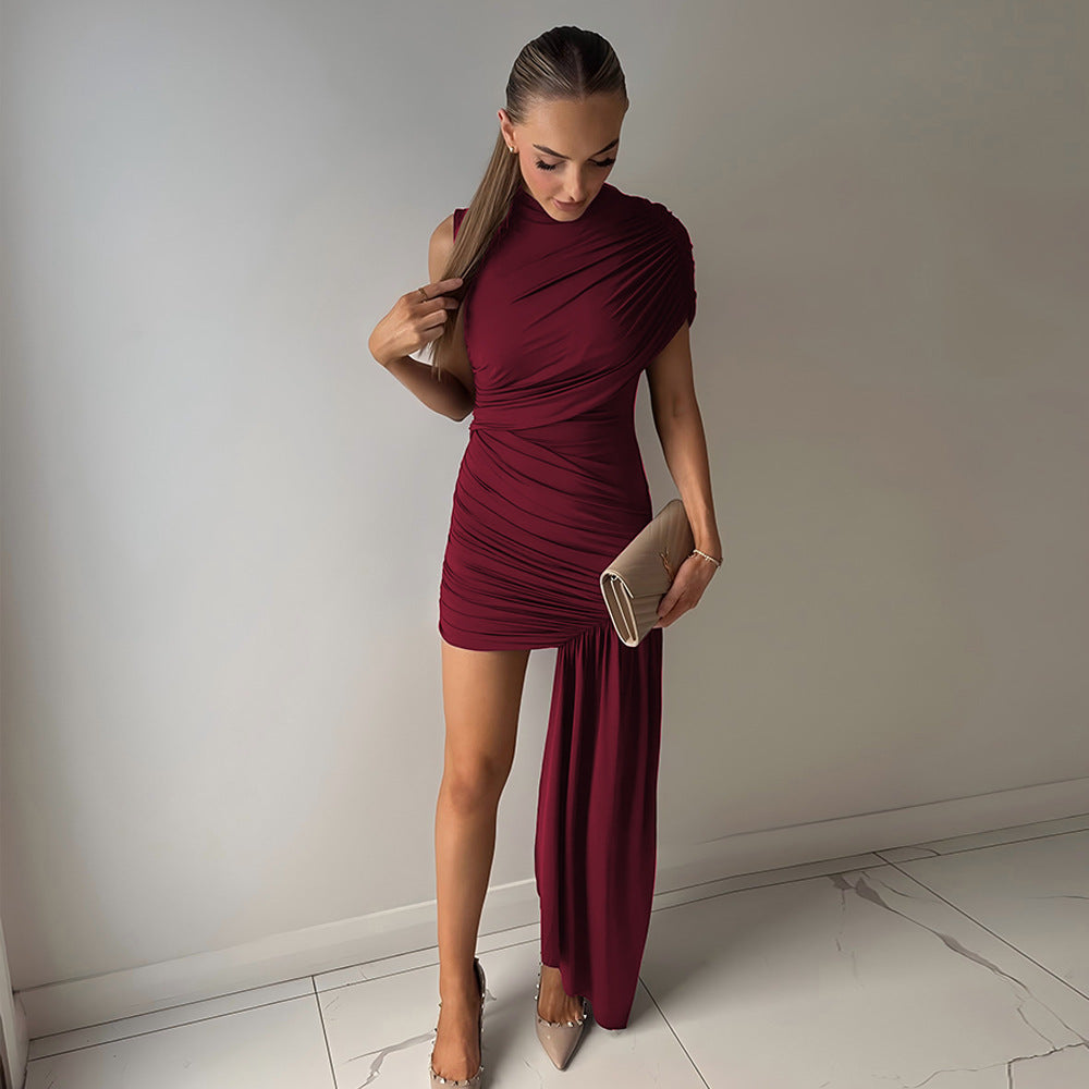 A woman in a burgundy draped dress with an asymmetrical hemline and a thigh-high slit, holding a clutch and looking down.