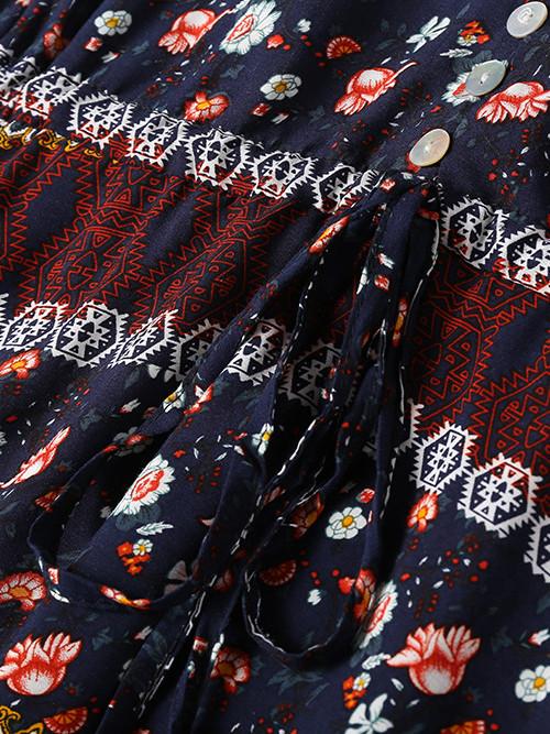 Close-up of a navy fabric with a floral and geometric print, featuring white buttons and a tie waist.