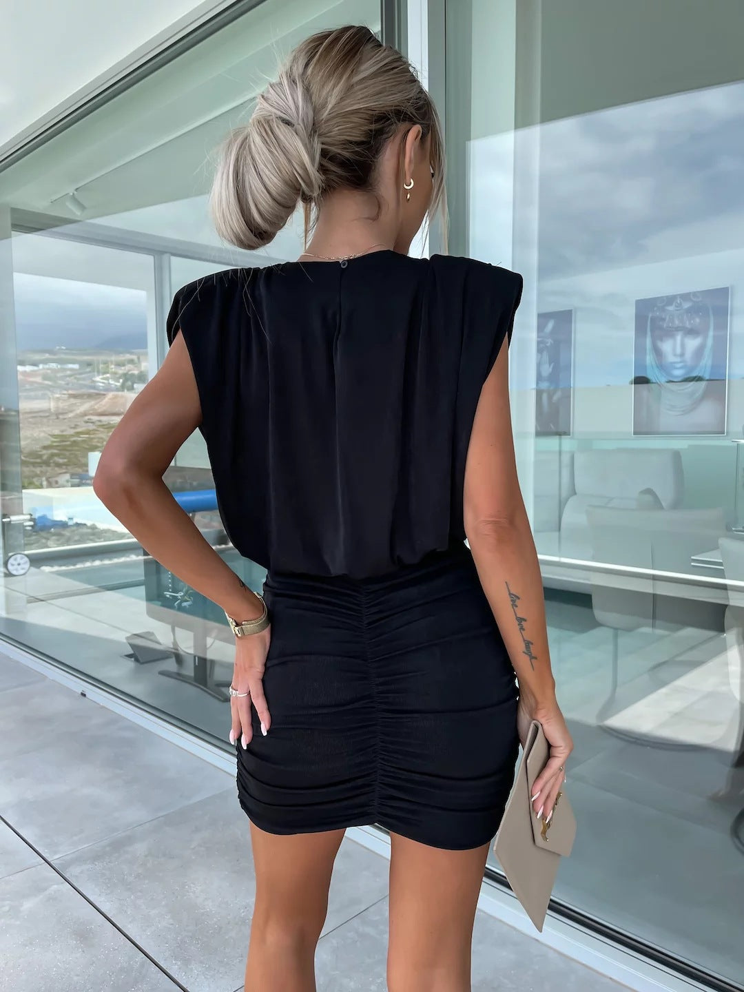 Close-up of a woman's back in a black mini dress with ruched detailing and padded shoulders.