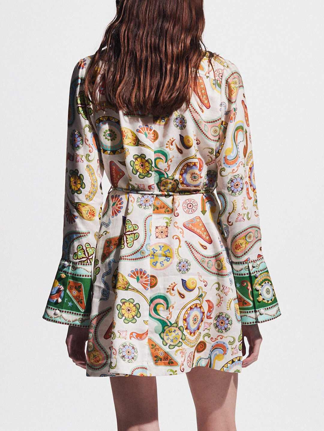 Back view of a woman wearing a white shirt dress with a colorful paisley print and bell sleeves.