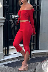 A woman in a red two-piece outfit, styled off-the-shoulder, poses outdoors. The outfit consists of a cropped top and capri pants with split hems.