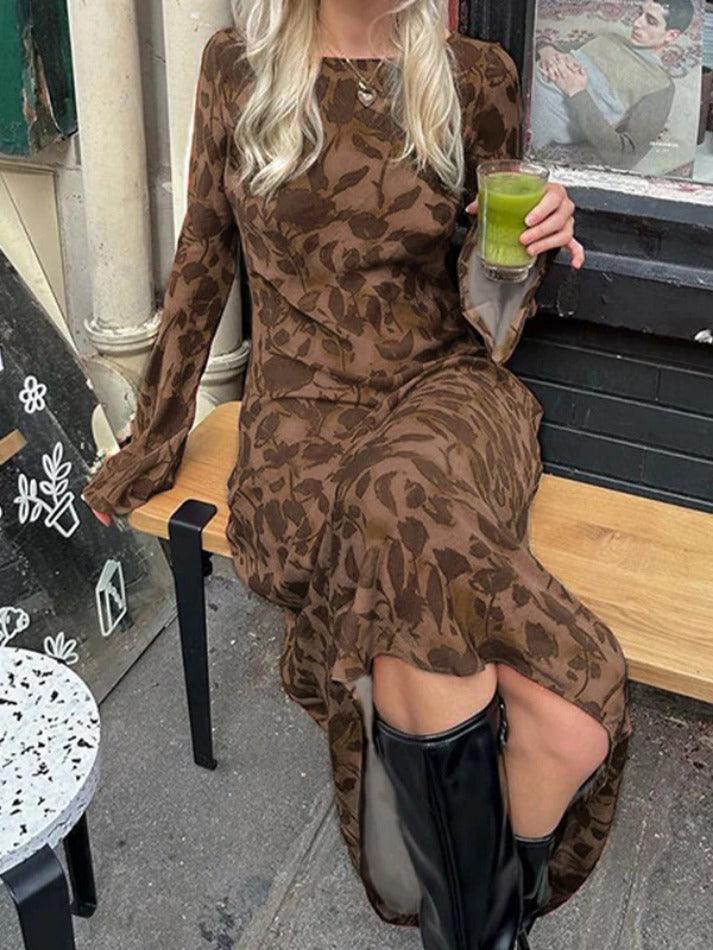 A woman in a brown floral maxi dress and black boots sitting on a bench and holding a green drink.