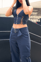 A close-up of a young woman's torso, showing her navy blue crop top with lace-up detailing and zipper, and matching cargo pants.