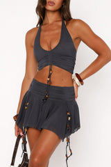 Close-up of a woman wearing a dark gray halter top and short skirt with beaded trim, accessorized with bracelets and holding a handbag.