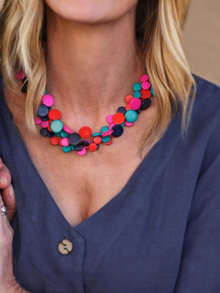 Close-up of a woman's neck and chest wearing a navy blue dress and a colorful, multi-layered beaded necklace.