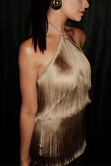 A woman in a gold fringe halter dress, side view