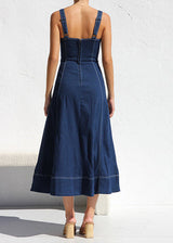 Back view of a woman in a dark blue denim midi dress, showing the zipper closure and the A-line skirt with contrast stitching.