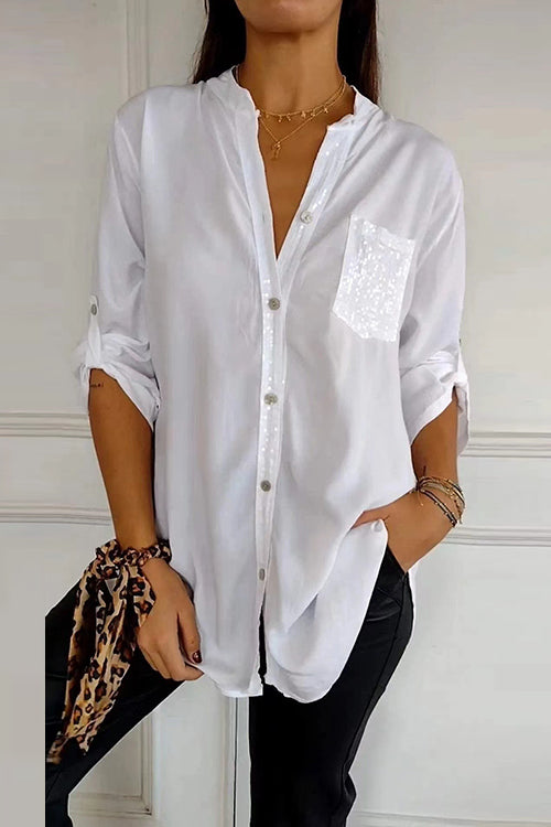 A woman wears a white long-sleeved shirt with a sequined pocket and black pants.