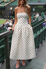Woman in a white and black polka dot strapless dress standing by a railing.