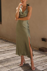 Woman in olive green satin slip dress with a halter neck and high slit, posing outdoors.