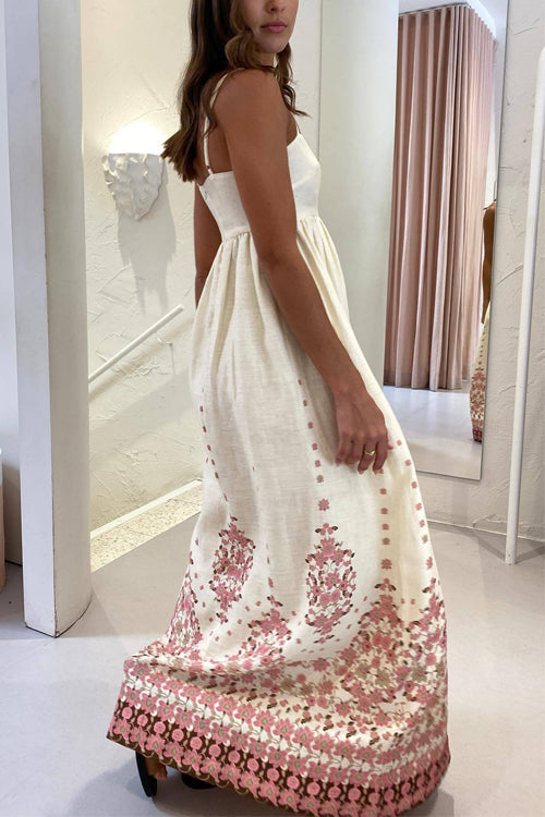 A woman from the side wearing a cream maxi dress with spaghetti straps and a pink floral print.