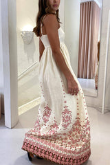 A woman from the side wearing a cream maxi dress with spaghetti straps and a pink floral print.