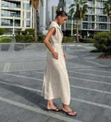 A woman in an ivory linen dress stands on a city sidewalk.