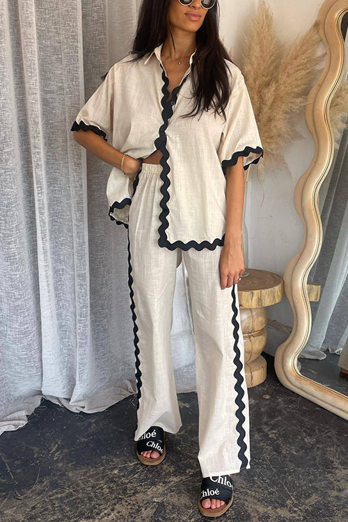 Woman wearing a cream linen-like pajama set with black scalloped trim, paired with a white crop top and black slides with 'Chloe' logo.