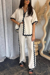 Woman wearing a cream linen-like pajama set with black scalloped trim, paired with a white crop top and black slides with 'Chloe' logo.