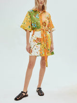 A woman wearing a short-sleeved, collared shirt dress with a floral print and a belted waist, paired with black sandals, standing against a white background.