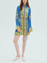 A woman stands in a blue shirt dress with a bold floral print and bell sleeves.
