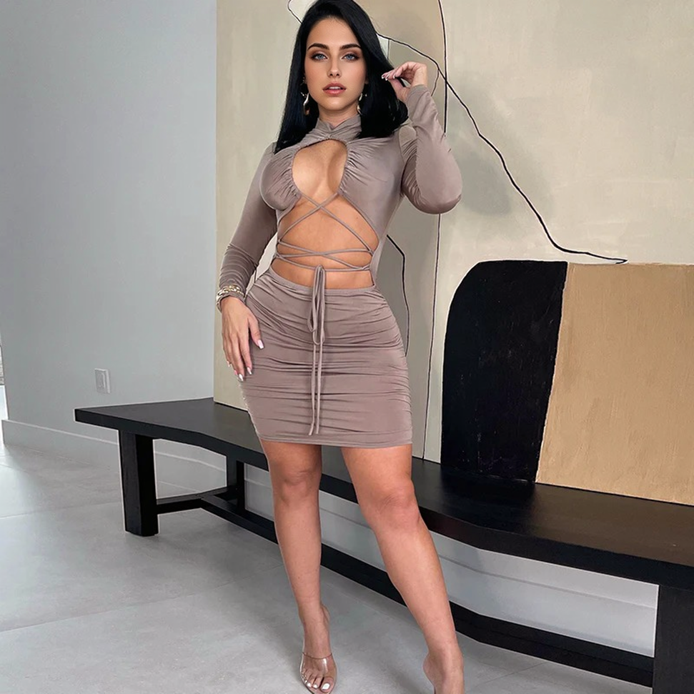 Woman in a brown long-sleeved, cut-out, lace-up, ruched mini dress posing indoors.
