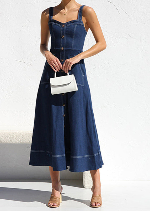 Woman in a dark blue denim midi dress with a sweetheart neckline, button-down front, and patch pockets, holding a white handbag.