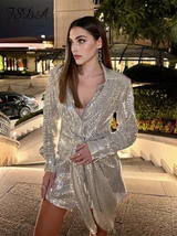 Woman in a shimmering silver sequined dress with a collared neckline and tie waist, standing on outdoor stairs at night.