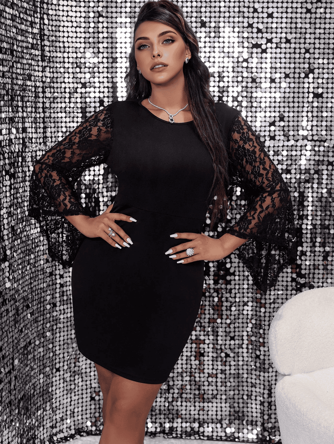 A woman in a black lace-sleeve dress stands with hands on hips.