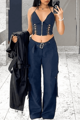 A young woman stands in an indoor space, holding a black jacket over her arm and posing for a photo with her phone.