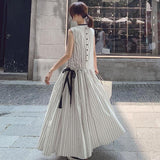 Woman wearing a long white sleeveless dress with black vertical stripes and a black ribbon tie at the waist, walking away from the camera.