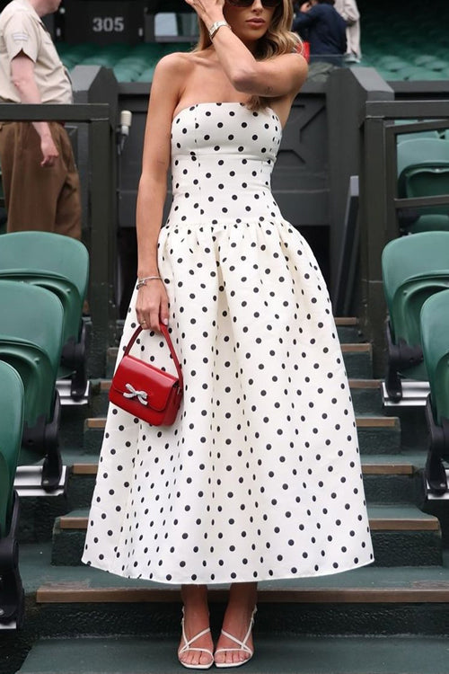 Woman in a white and black polka dot strapless dress holding a red handbag.