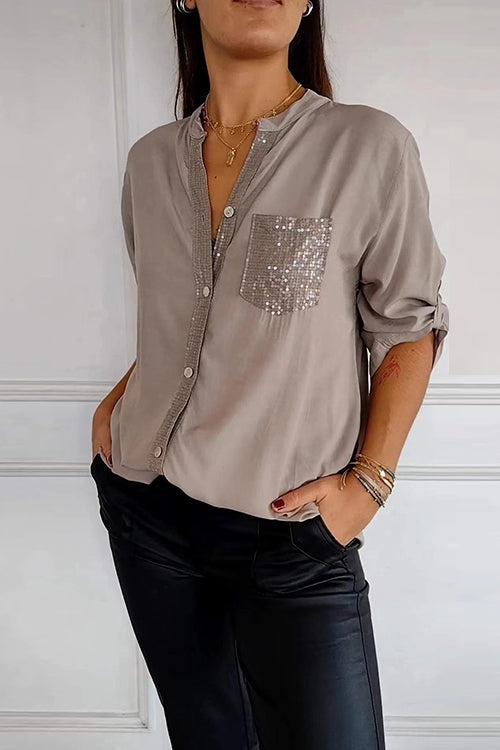A woman wears a grey long-sleeved shirt with a sequined pocket and black pants.