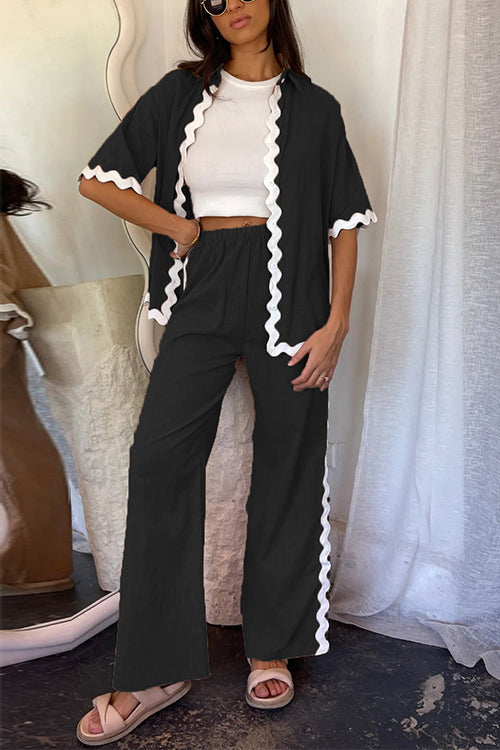 Woman wearing a black linen-like pajama set with white scalloped trim, paired with a white crop top and beige sandals.