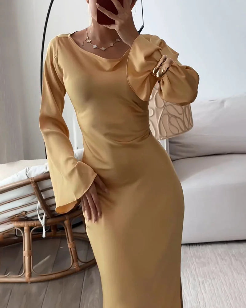Woman in a gold satin dress with long bell sleeves, looking at her reflection in a mirror.