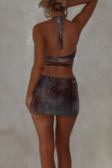 Rear view of a woman in a halter top and mini skirt with a purple and grey tie-dye print.