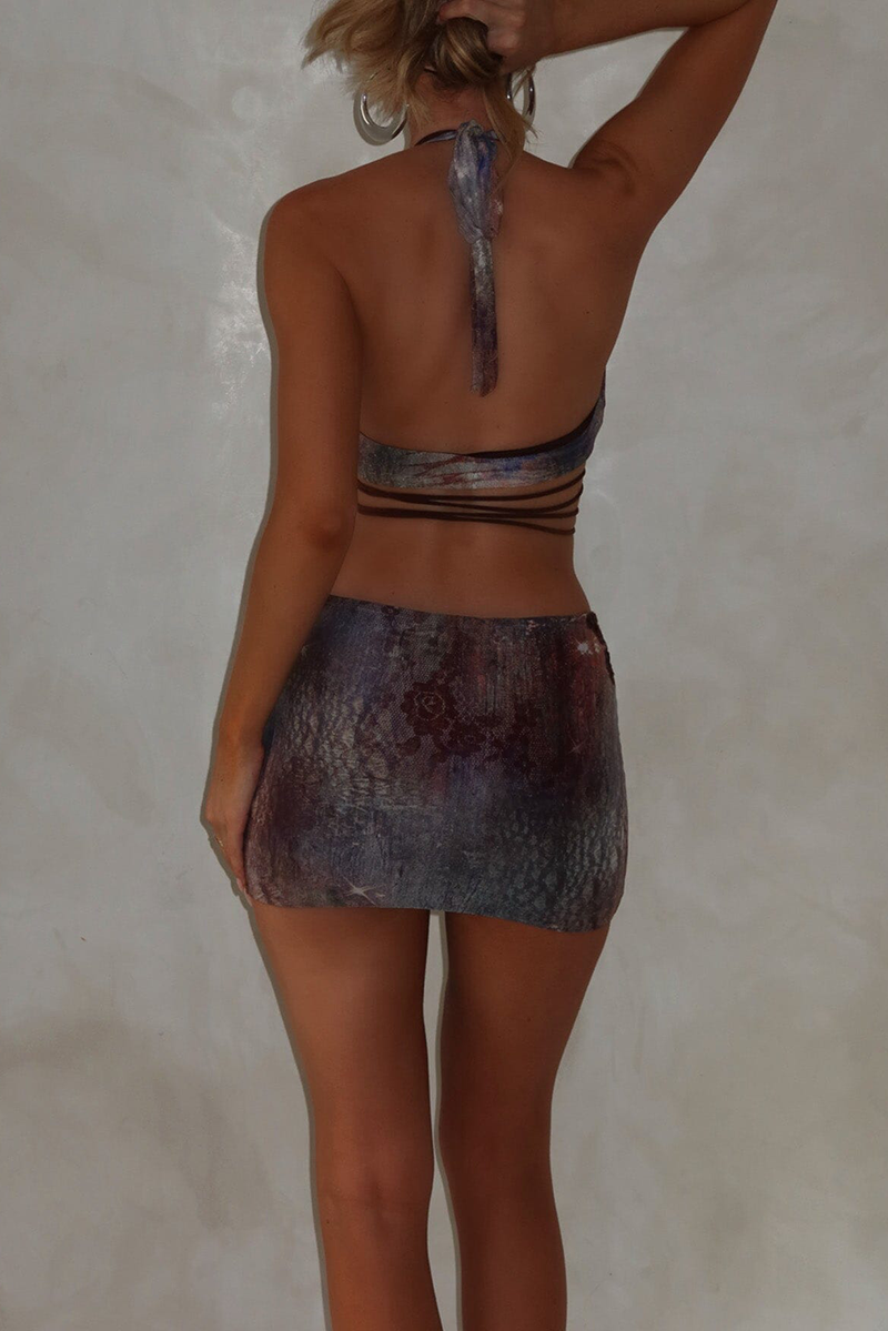 Rear view of a woman in a halter top and mini skirt with a purple and grey tie-dye print.