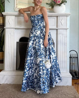 Woman wearing a strapless blue and white floral print ball gown, leaning against a fireplace.