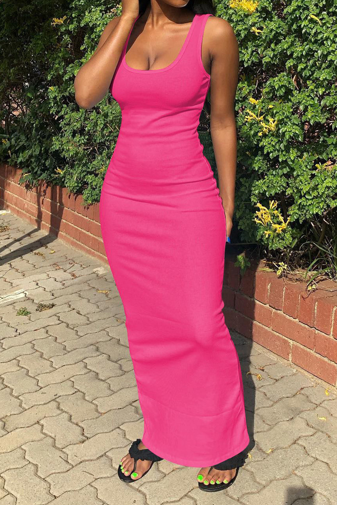 A woman wearing a bright pink sleeveless ribbed bodycon maxi dress with a scoop neck, standing outdoors.