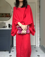 Woman in a red linen dress holding a purple clutch.