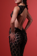 Back view of a woman in a black lace outfit, showcasing an open back and ruched detailing on the pants, with a red background.