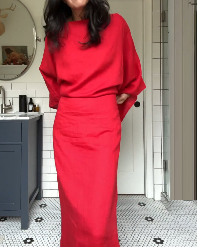 Woman in a red linen dress with kimono sleeves, hands on hips, in a bathroom.