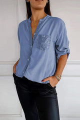 A woman wears a blue long-sleeved shirt with a sequined pocket and black pants.