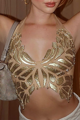 A woman wearing a gold sequined butterfly halter top and white pants, holding a gray purse.