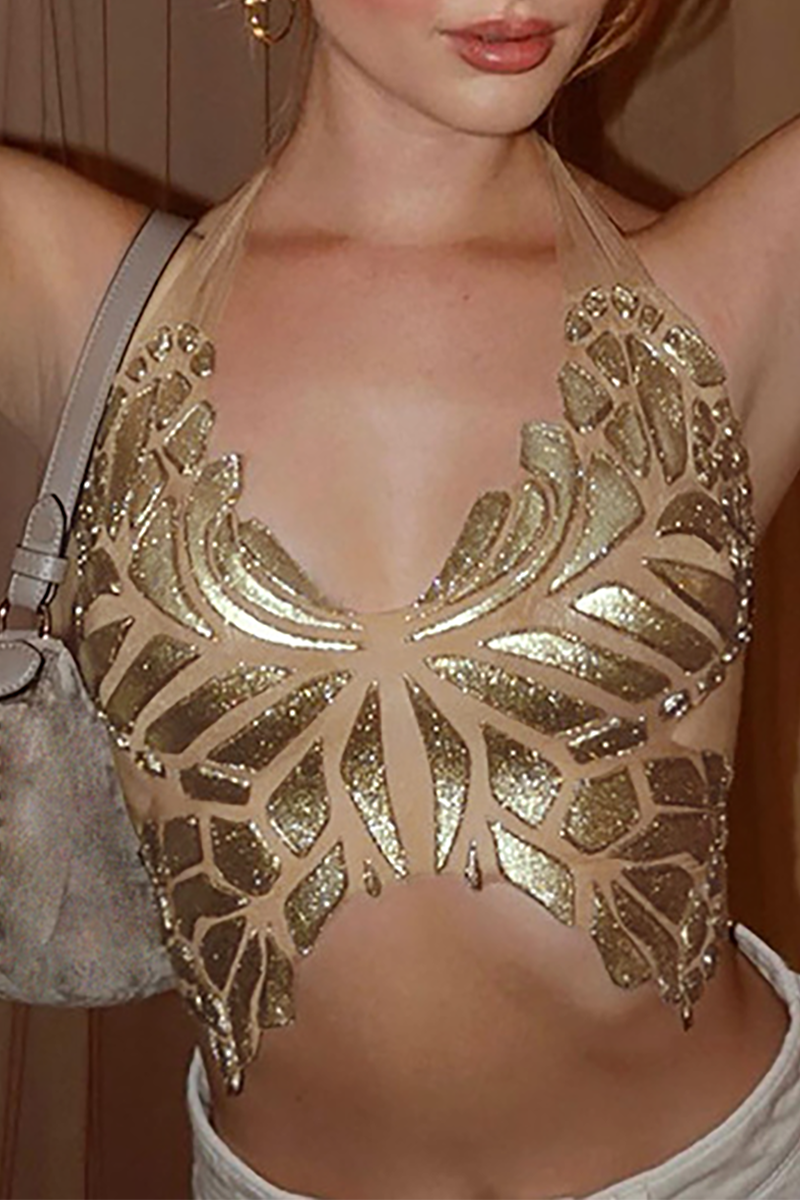 A woman wearing a gold sequined butterfly halter top and white pants, holding a gray purse.