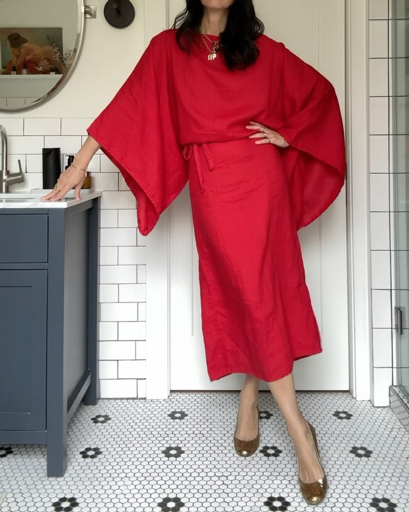 Woman wearing a red linen dress with kimono sleeves and gold heels, standing next to a vanity.
