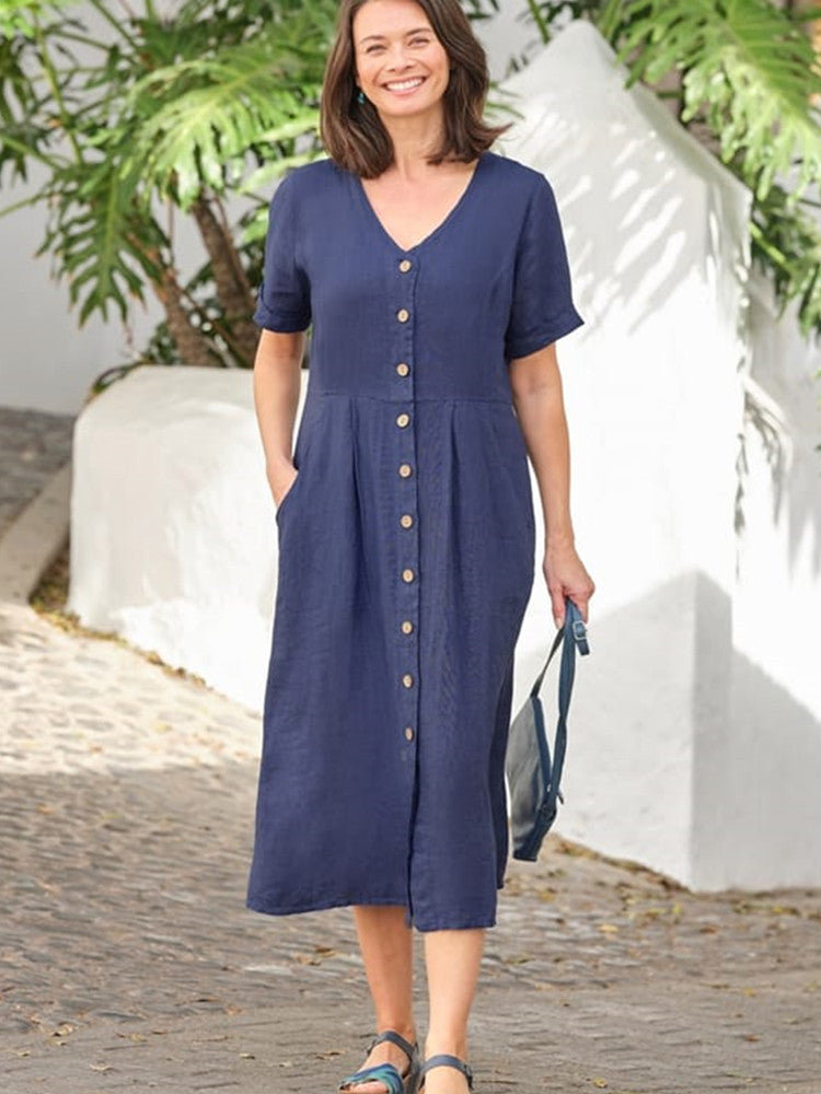 Woman wearing a navy blue linen midi dress with a button-down front and short sleeves. She is smiling and holding a dark blue bag.