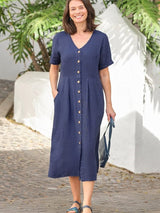 Woman wearing a navy blue linen midi dress with a button-down front and short sleeves. She is smiling and holding a dark blue bag.
