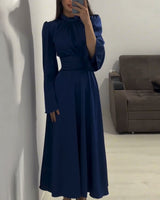 Woman wearing a long, navy blue satin dress with bell sleeves and a wide belt, standing in front of a mirror, showing the full length of the dress.