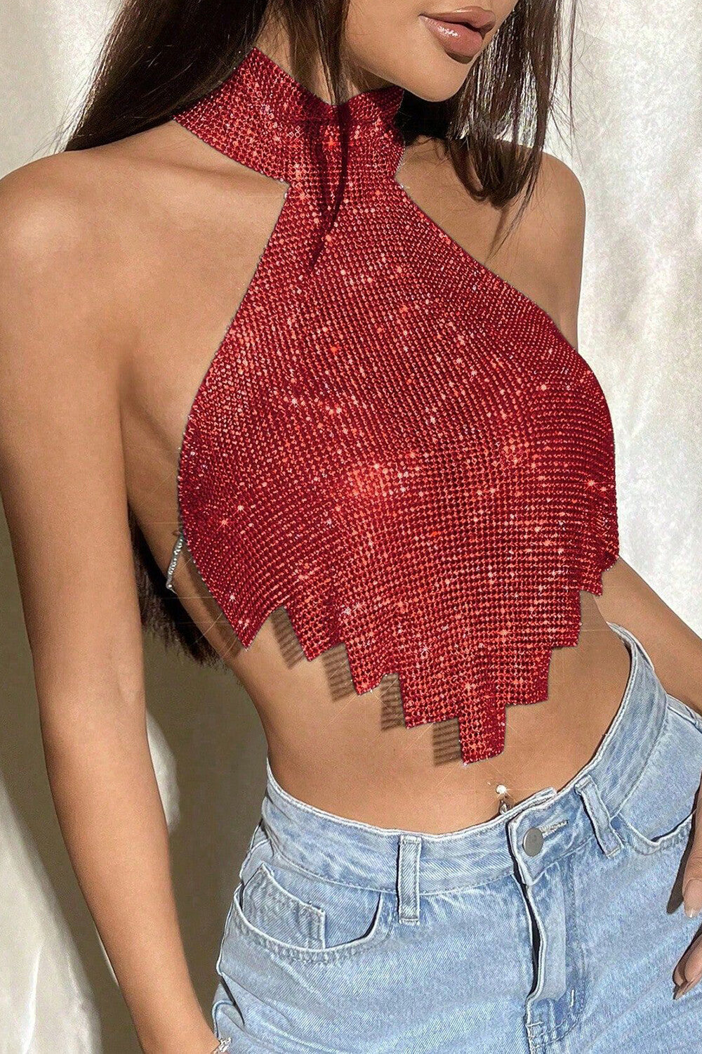 A woman from the side wearing a red halter top with a fringe hem and light-wash jeans.