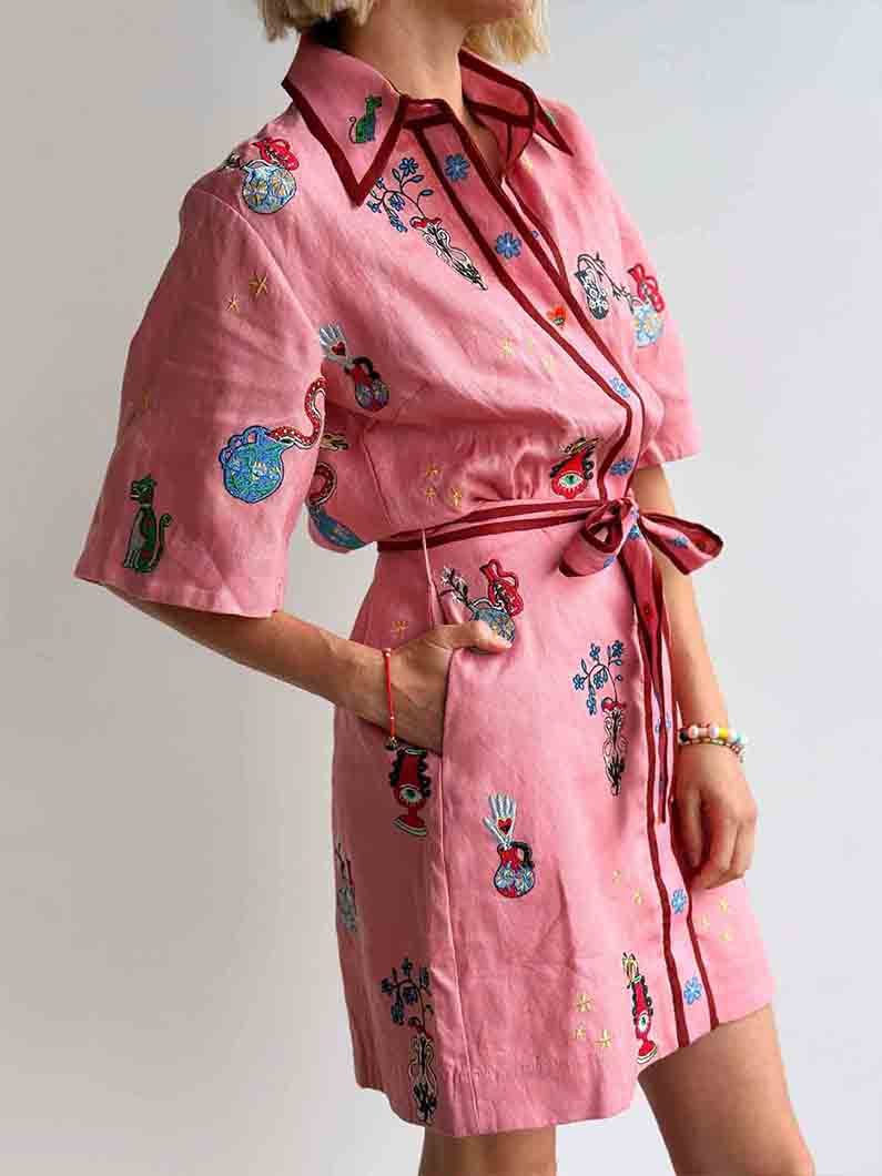 Close-up of a woman's torso in a pink shirt dress with embroidered designs and pockets.