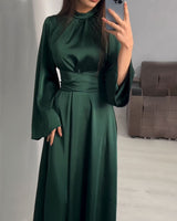 Close-up of a woman wearing a dark green satin dress with a high neckline and bell sleeves, holding a phone.