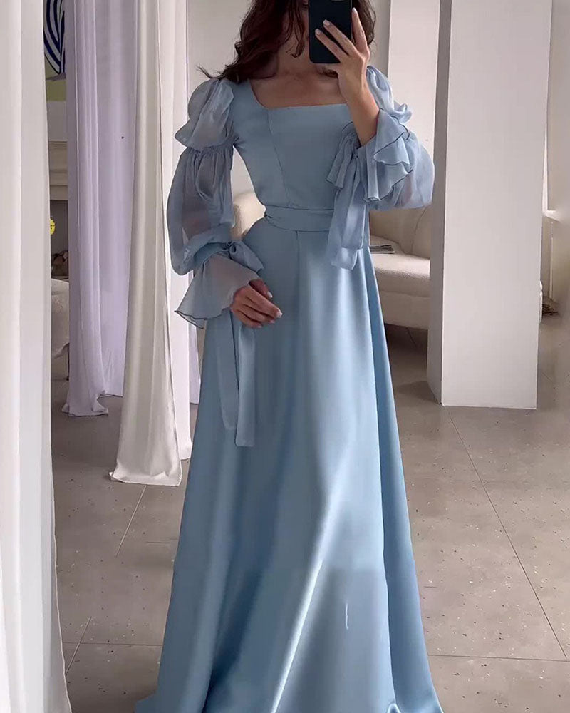 A woman in a light blue satin dress with dramatic puff sleeves and a square neckline is taking a mirror selfie.
