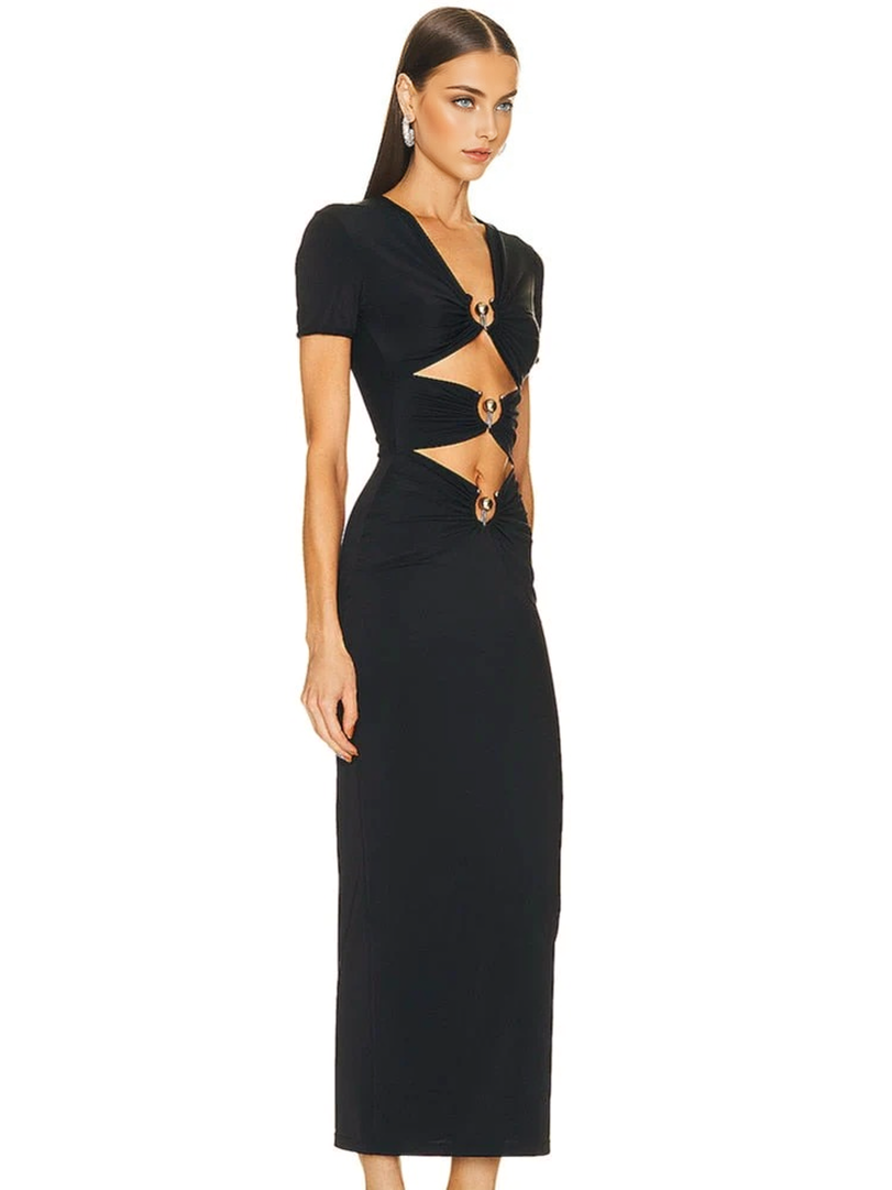 A woman wearing a black, floor-length dress with short sleeves and cutouts at the waist and chest, accented with gold rings. She is shown in a profile view.